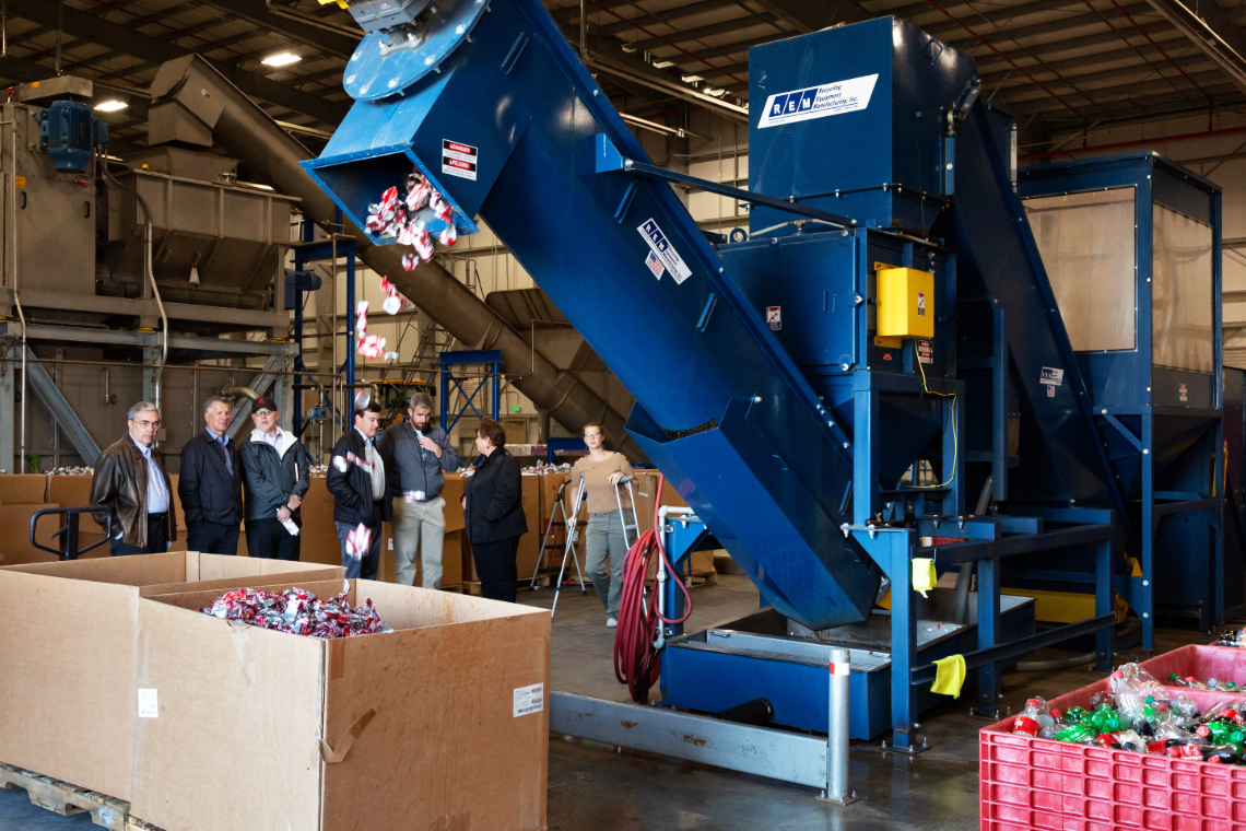 Jack Pelo, President and CEO of Swire Coca-Cola, USA (center) inspects the processing of out-of-date and damaged product.